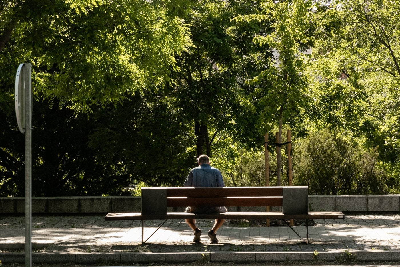 Un hombre en edad de jubilación descansa al sol sentando en el banco de un parque.