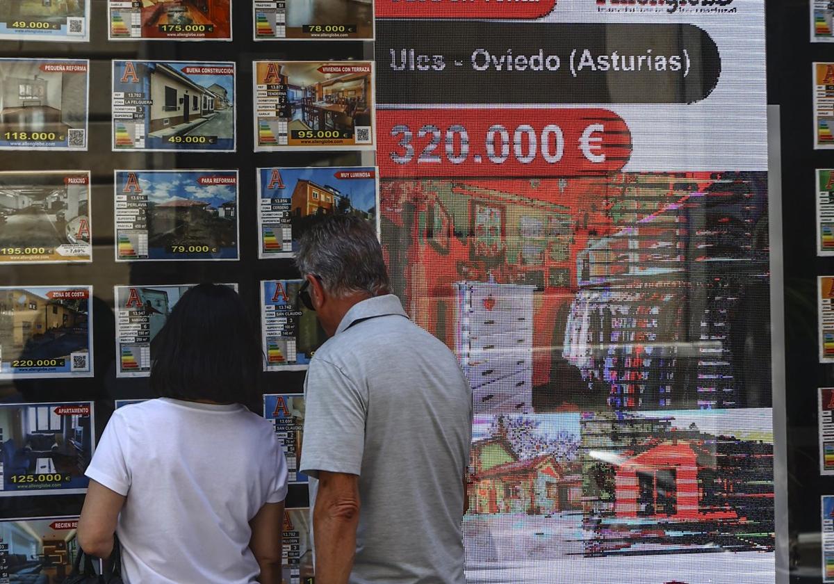 Una pareja comprueba las ofertas de vivienda disponibles en una agencia inmobiliaria de Oviedo.