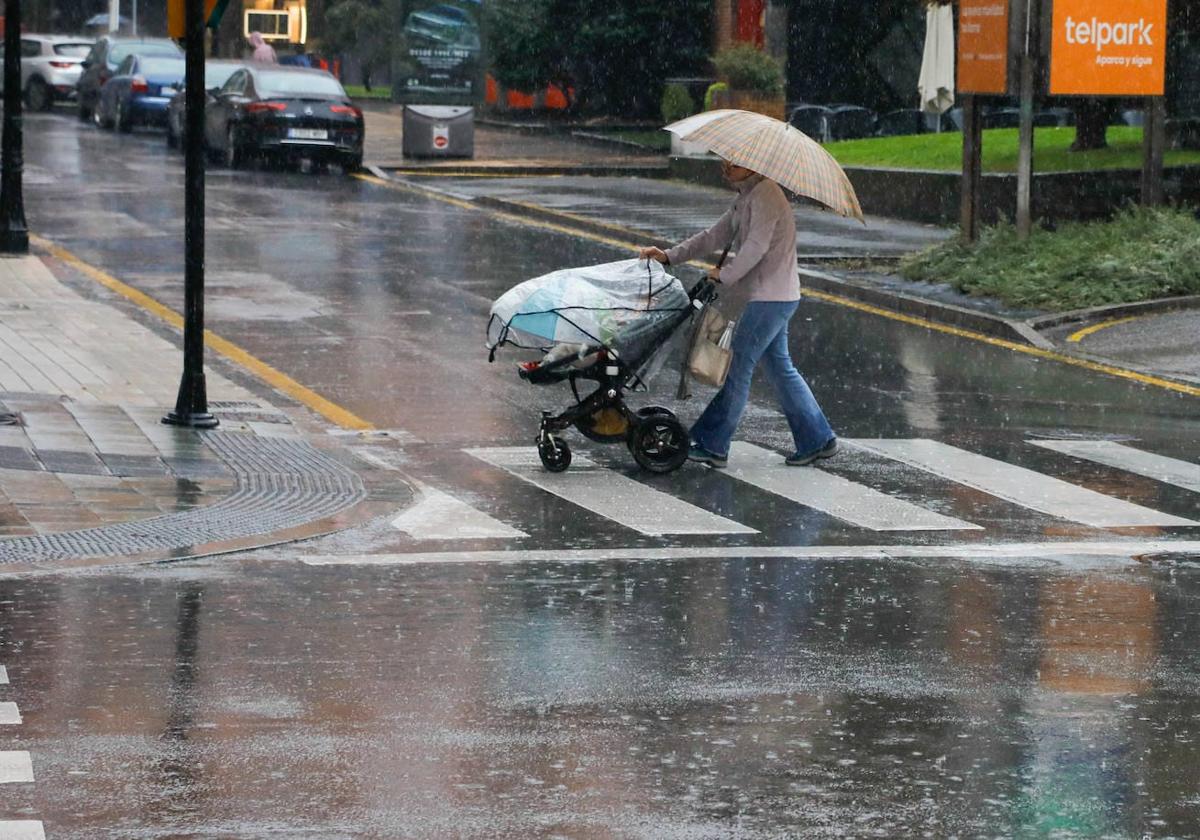 Una mujer pasea con su bebé durante las constantes lluvias caídas el pasado miércoles en Gijón.