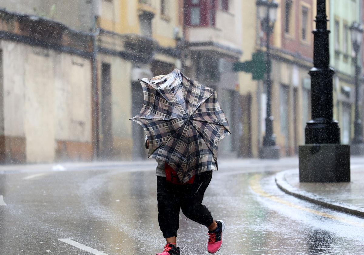 Una mujer intenta caminar en Oviedo, bajo la lluvia e intensas rachas de viento.