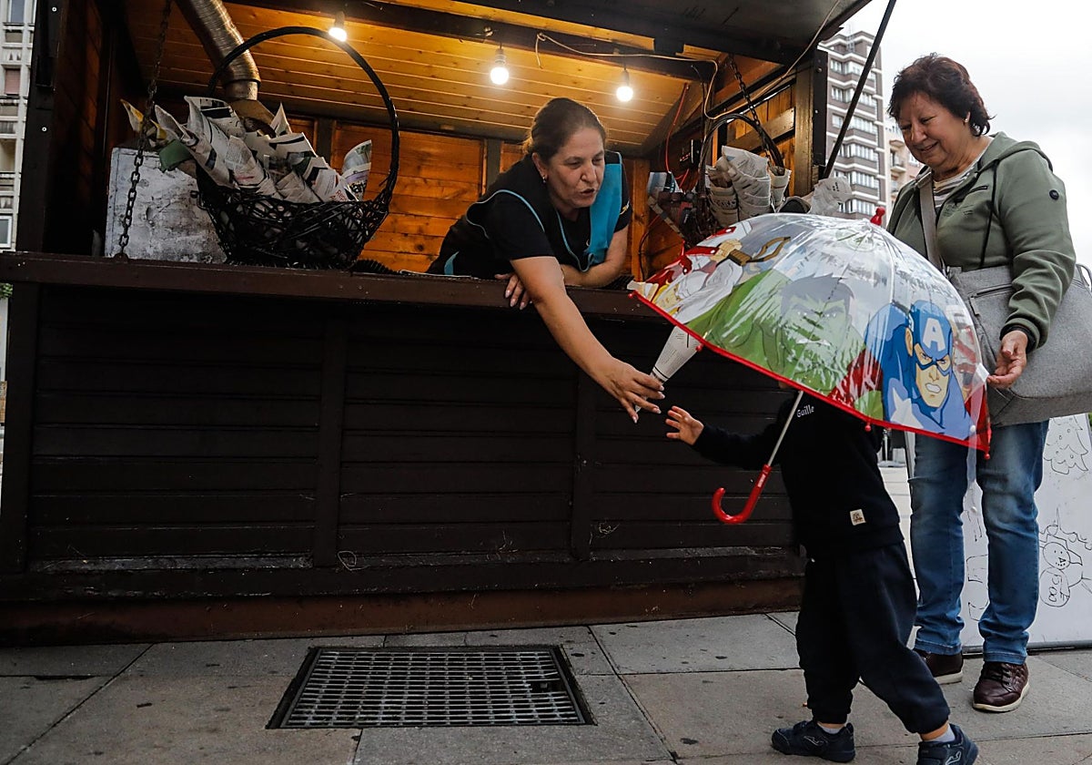 Berta González le entrega un cucurucho de castañas asadas al pequeño Guille, de dos años, en el puesto de la plaza del Seis de Agosto, ante la mirada de su abuela, Modes Melchor