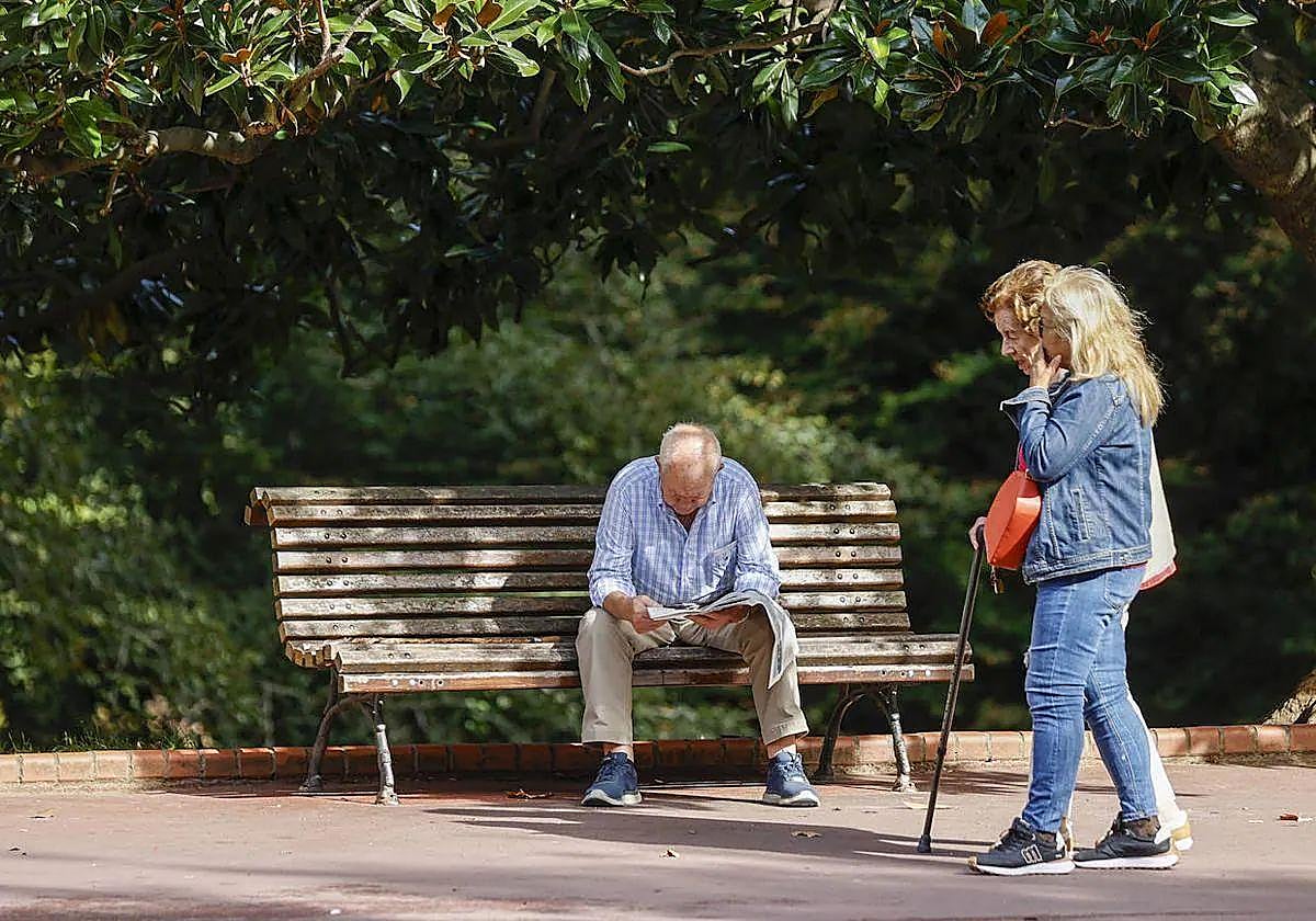 Un hombre lee un periódico mientras dos mujeres pasean.