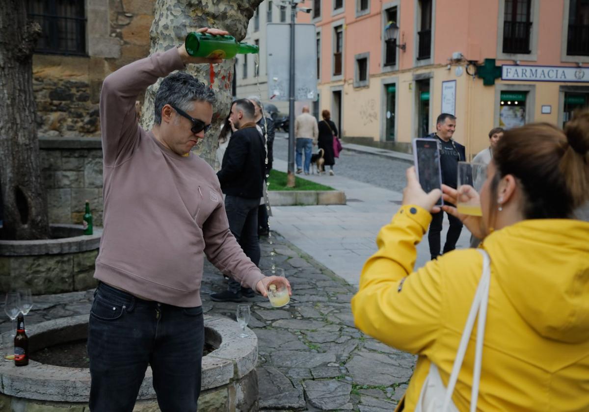 Una mujer saca una foto a su acompañante, que escancia un culín de sidra en la plaza de Jovellanos, en el barrio gijonés de Cimavilla.