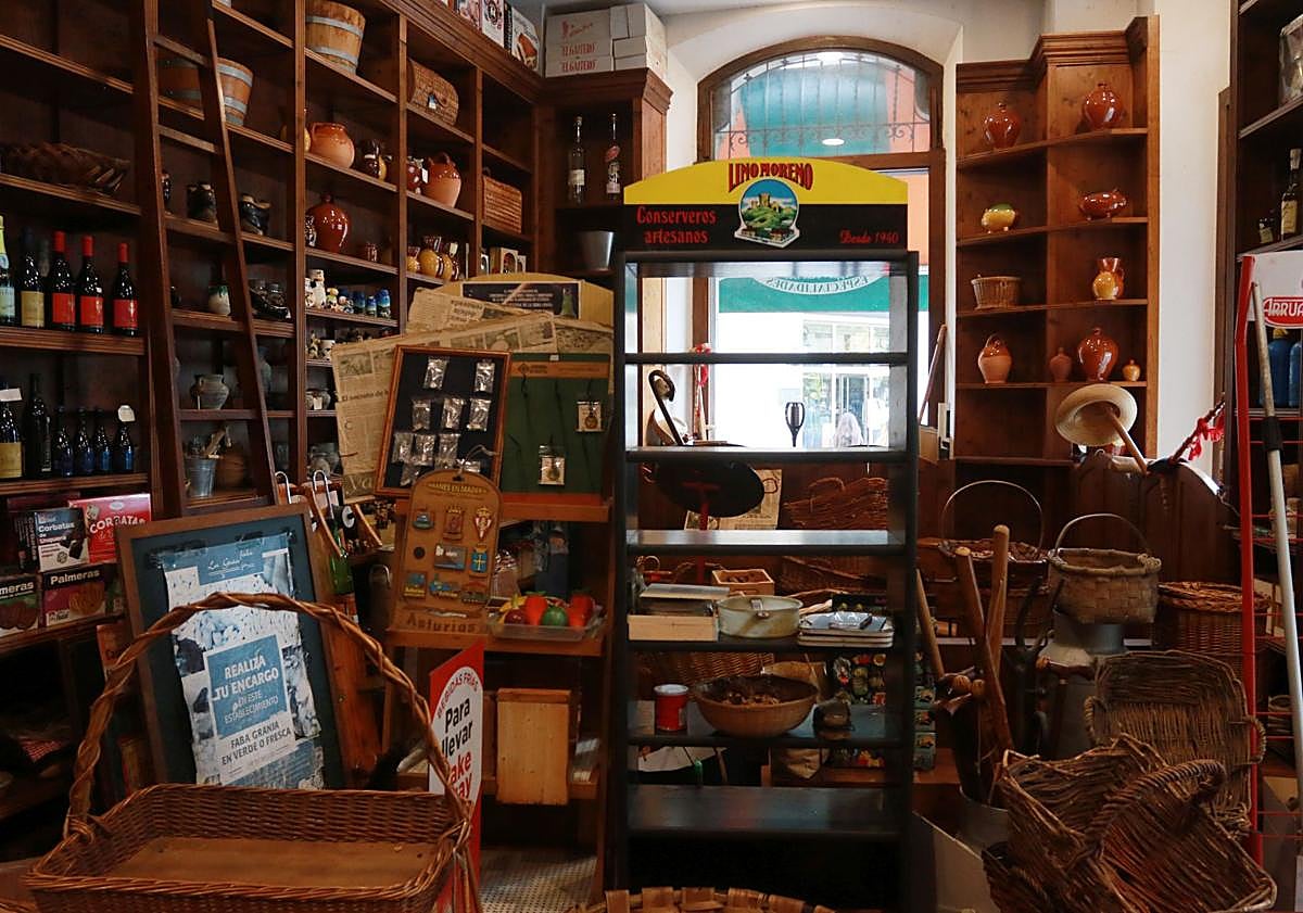 Imagen principal - Arriba, estanterías repletas aún de objetos; a la izquierda, paellera con imanes, cestería y escanciadores y a la derecha, imanes asturianos y al fondo una lechera tradicional. 