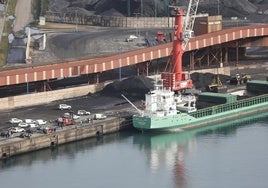 Un carguero, atracado en el muelle Olano del puerto de El Musel, en Gijón, junto al carbón que almacena en sus instalaciones Lissan Coal.