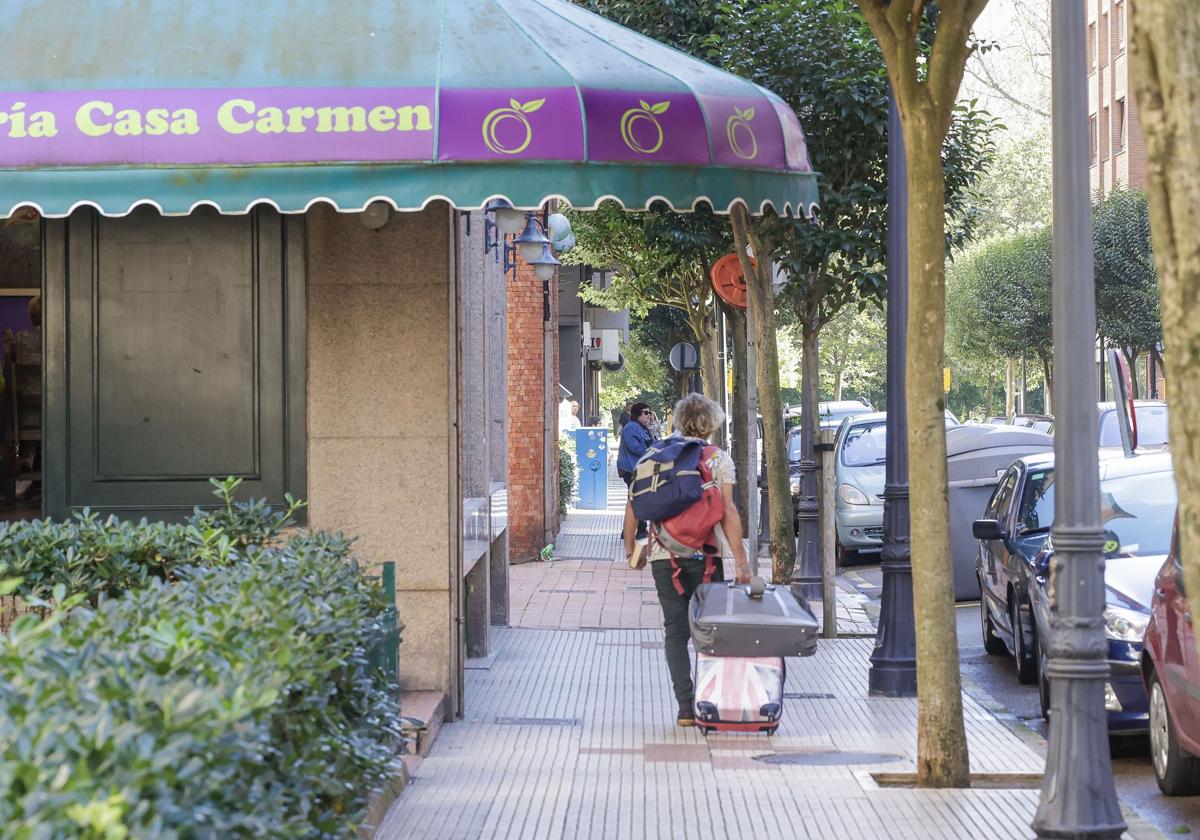 Un visitante de Gijón, con maletas, por la calle Doctor Aquilino Hurlé, en La Arena, barrio que será declarado zona tensionada junto con Cimavilla.