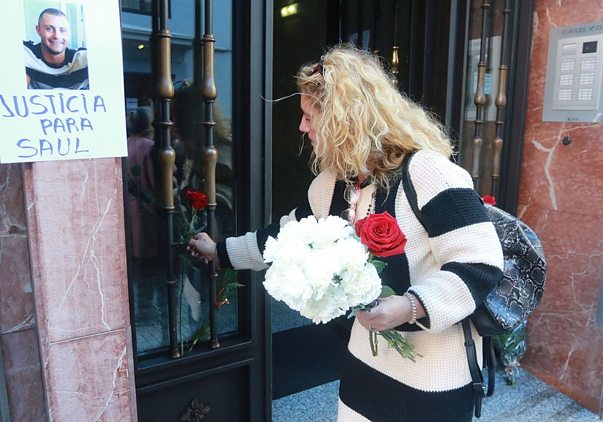 Carmen Iglesias, la madre de Saúl, coloca flores en el edificio de la calle Avilés, en Gijón, donde murió su hijo en 2023