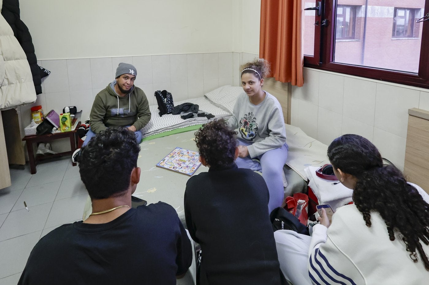 Tommys Herrera y Roxana Lewis juegan al parchís con sus hijos en su habitación del Albergue.