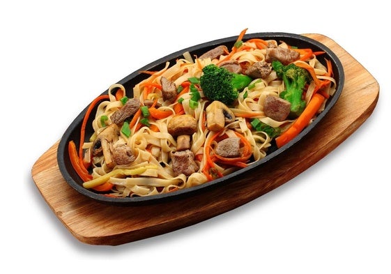 Udon con carne, verduras y champiñones en un plato de piedra aislado sobre fondo blanco.