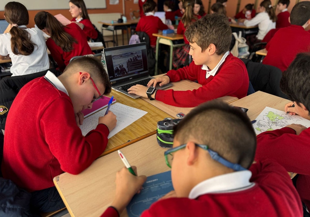 Varios alumnos trabajan con el papel y el chrombook en un aula.