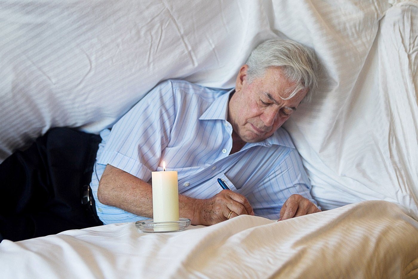Mario Vargas Llosa escribe a mano en la cama iluminado por una vela.