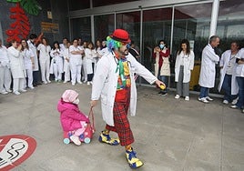 Uno de los payasos lleva a una niña en un juguete a las puertas de Pediaría del HUCA.