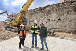 Noelia Fernández y Alejandro García conversan con el concejal Pelayo García ante un tramo de muralla descubierto.