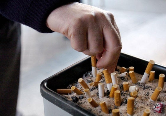 Una persona apaga un cigarrillo en un cenicero ubicado en la calle.