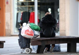 Una mujer sin recursos, descansa en un banco con todas sus posesiones en un carrito y en bolsas.