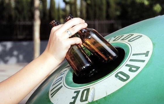 Un ciudadano introduce dos botellas de vidrio en un contenedor.