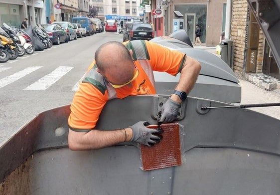 Un operario de Emulsa instalando una placa antiolor en un depósito de residuos orgánicos y resto de la ciudad.