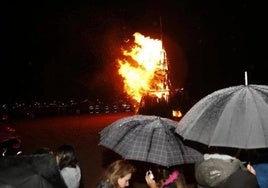Los vecinos, bajo el paraguas, contemplan el fuego en la playa de Poniente, en Gijón.