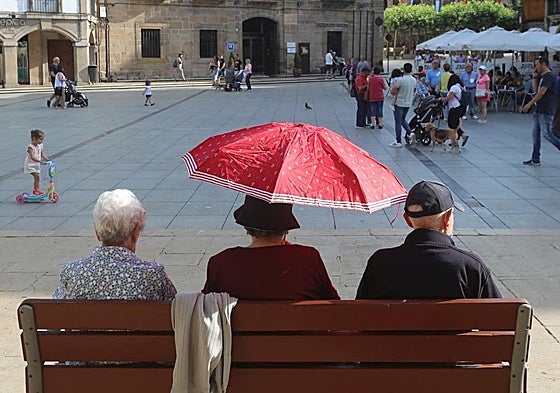 Tres personas de edad avanzada se protegen del calor en la plaza de España de Avilés.