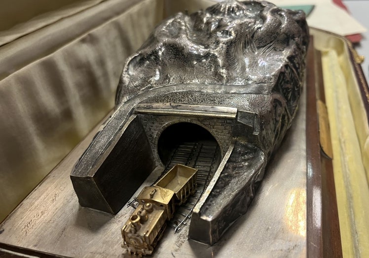 Maqueta ferroviaria con el túnel en plata y la locomotora y el vagón en oro.
