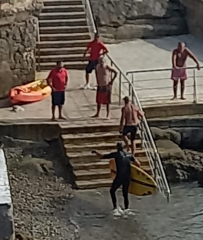 Imagen secundaria 2 - Arriba, momento del rescate del vecino de Cimadevilla de 54 años en la mar a la altura del Club de Regatas. Debajo, S. P. J. se abraza a su rescatador y más abajo, ya escaleras arriba, con bañador rojo.