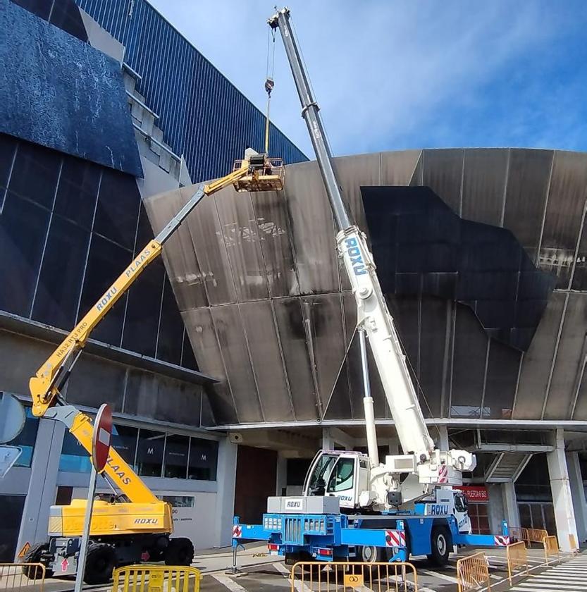 Una grúa y una plataforma elevadora durante los trabajos realizados este mediodía para retirar el módulo vertical de la fachada textil en la grada norte. A la izquierda la pieza oblicua desmontada de la grada este.