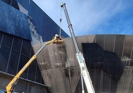 Una grúa y una plataforma elevadora durante los trabajos realizados este mediodía para retirar el módulo vertical de la fachada textil en la grada norte. A la izquierda la pieza oblicua desmontada de la grada este.