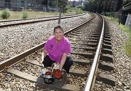 Pilar Meana, con una fabada en su olla ferroviaria, posa en las vías del tren junto a su negocio.