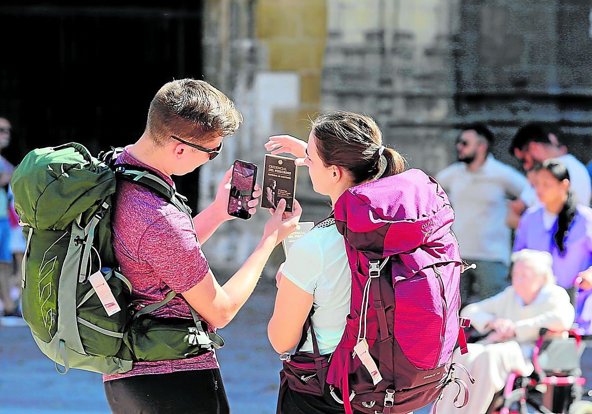Dos peregrinos, con las mochilas a sus espaldas, sacan una foto a la credencial que acredita su paso por la Catedral de San Salvador.