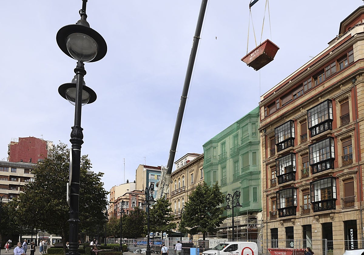 Una grúa eleva un contenedor de obra para los trabajos de reforma del teatro Jovellanos, de Gijón.