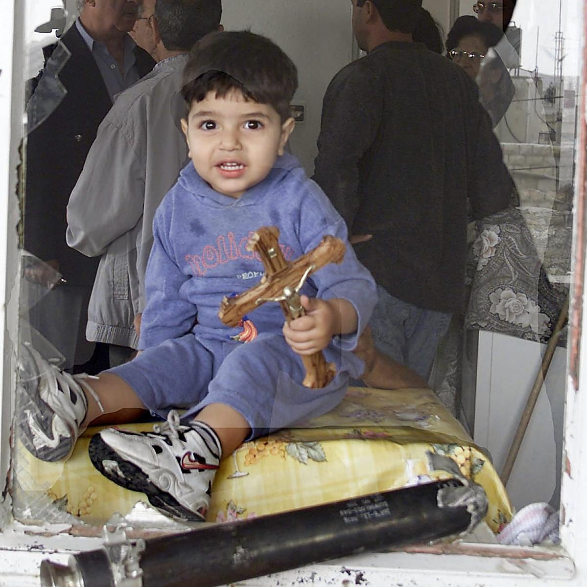 Un niño cerca de Belén, con una cruz, entre escombros y restos de artillería.