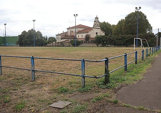 Vista del campo de fútbol situado en los terrenos propiedad del Puerto en Jove, con la iglesia de la Santa Cruz al fondo.