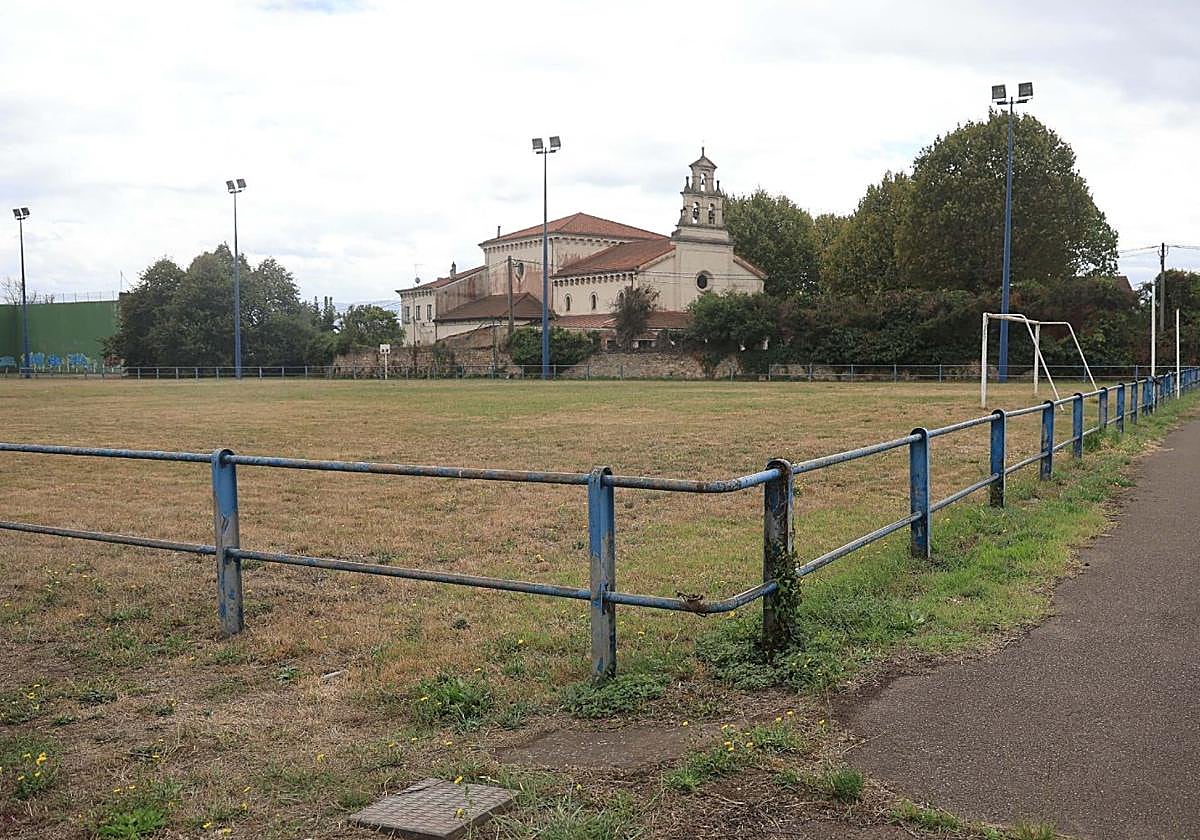 Vista del campo de fútbol situado en los terrenos propiedad del Puerto en Jove, con la iglesia de la Santa Cruz al fondo.