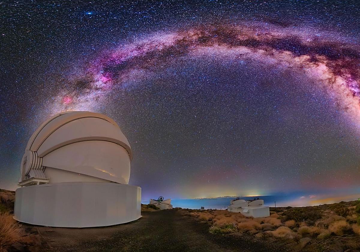 El Two-meter Twin Telescope (TTT), que se compone de varios edificios en el Teide, bajo una imagen de larga exposición de la Vía Láctea.