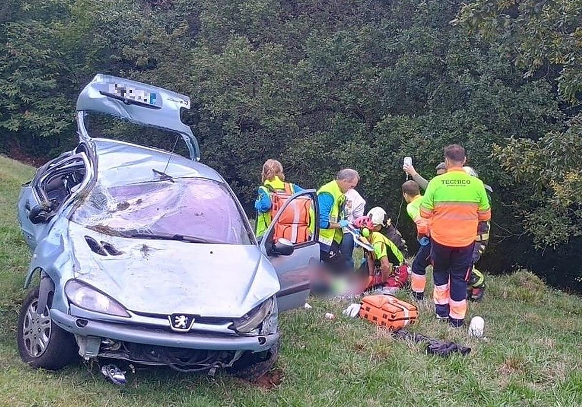 Los sanitarios atienden a los heridos tras caer el turismo carretera abajo en Las Regueras.