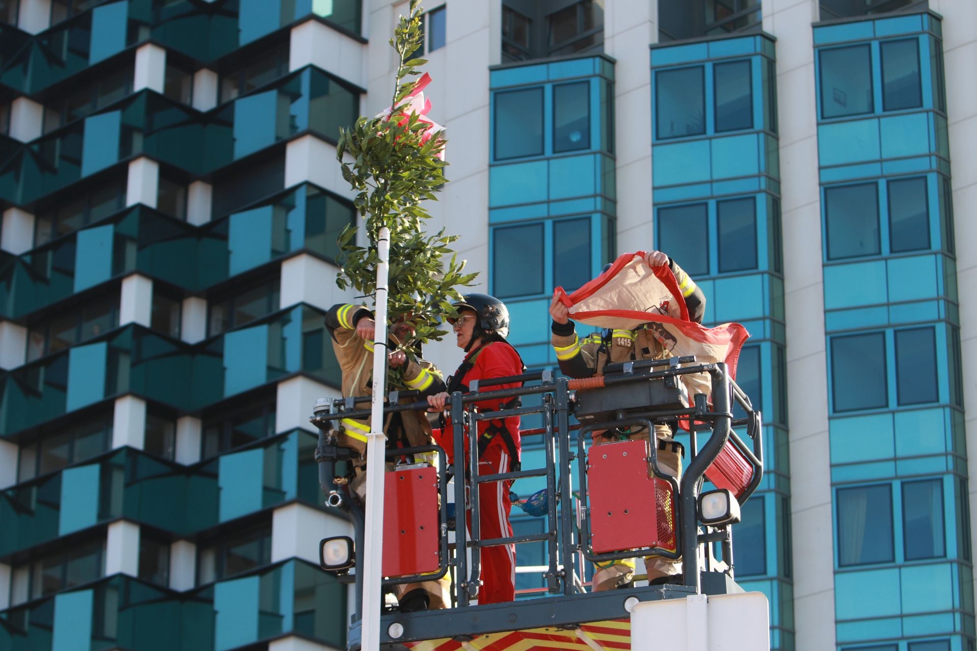 Carolina Méndez, con la ayuda de dos bomberos, cuelga el ramo de laurel en la escalera 12.