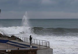 Un hombre pesca durante una jornada con fuerte oleaje en Gijón.