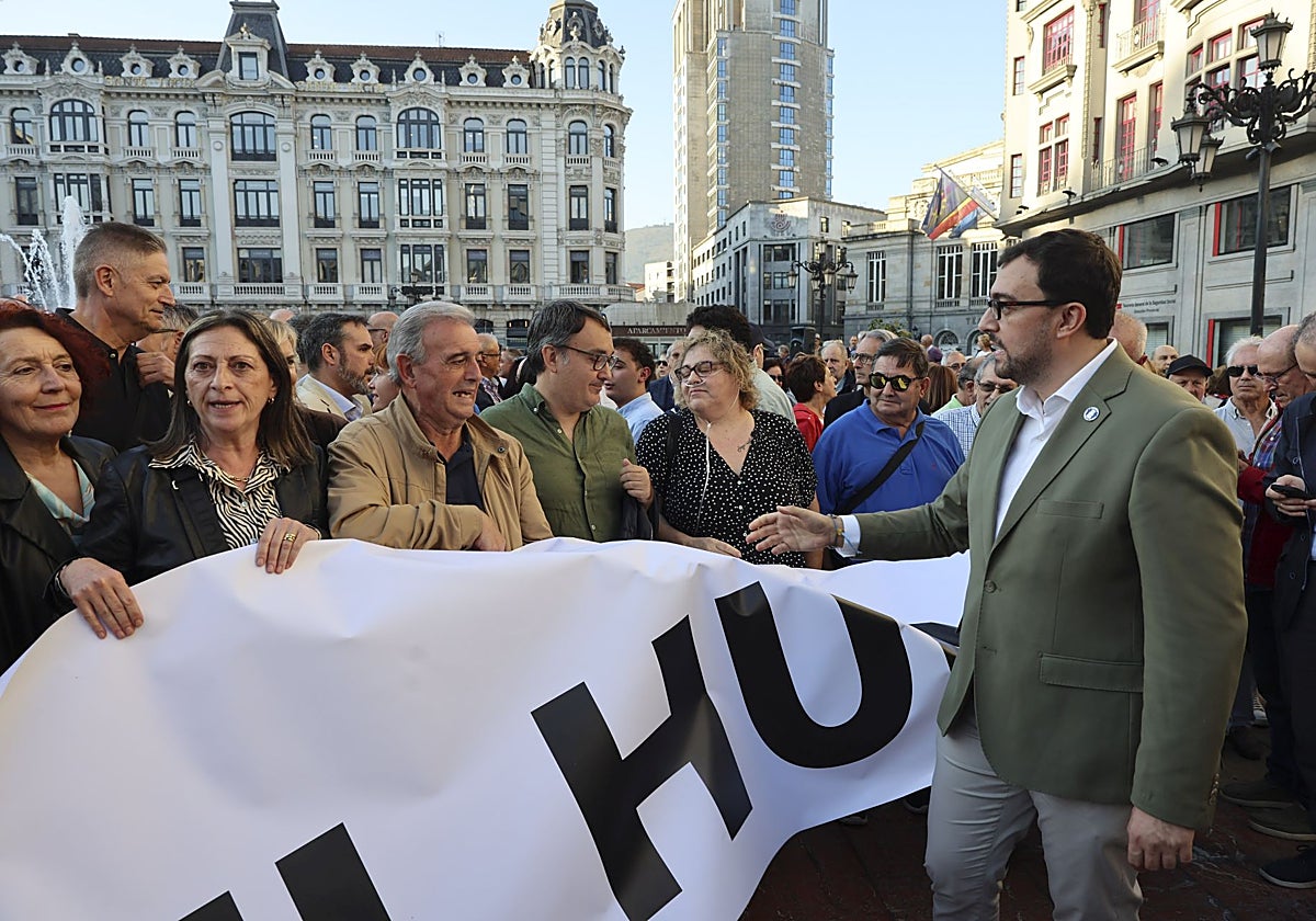 Dacio Alonso, presidente de UCE, portado la pancarta contra el peaje mientras el presidente Adrián Barbón le dirige un saludo.