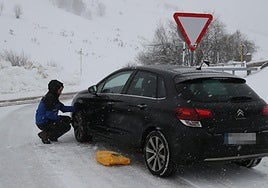 Un conductor pone cadenas a su vehículo en una vía secundaria de Asturias.
