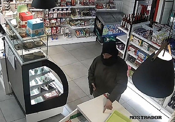 El atracador amenaza con el arma a un empleado para que deje el móvil en el mostrador.