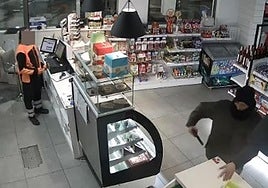 El atracador amenaza con el arma a un empleado para que deje el móvil en el mostrador.