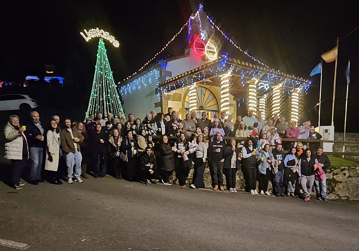 Vecinos de Llantones posan frente a la capilla del Carmen, con la alegre iluminación navideña tras ellos.