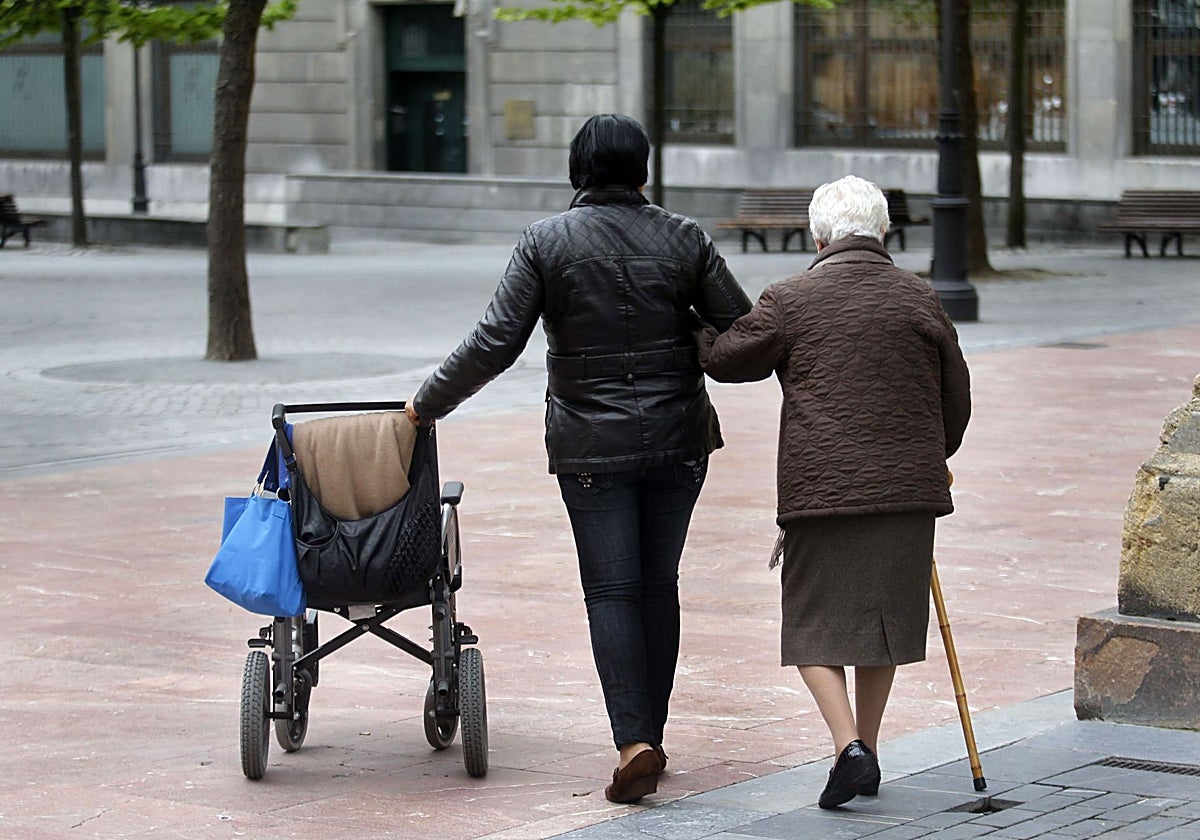 Una anciana pasea con su cuidadora por el centro de Oviedo, imagen que acompaña la noticia.