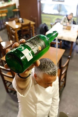 Un camarero escancia un culín de sidra en una sidrería.
