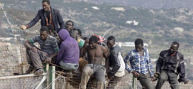 Inmigrantes de origen subsahariano, en la parte alta de la valla de Melilla. / Efe