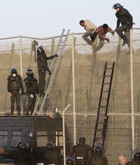 Agentes de la Policía, junto a inmigrantes encaramados en la valla.