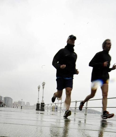 Dos hombres corren por el Muro de San Lorenzo, en Gijón. 