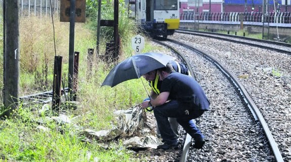 Dos agentes de la Policía Nacional observan los restos mortales de J. A. G. A. En segundo plano, el convoy de Feve detenido tras el accidente. 