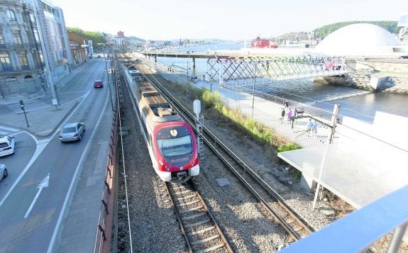 Un tren de Cercanías de Renfe pasa bajo la pasarela de acceso al Centro Niemeyer, entre la calle de El Muelle y la ría. 