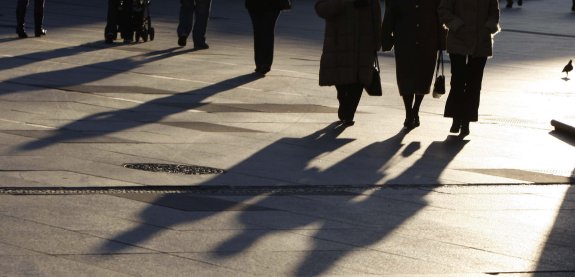Sombras proyectadas sobre el pavimento de la plaza de España, por donde pasea un grupo de personas de distintas edades. 
